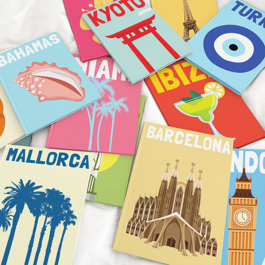 Colourful personalised travel photo books displayed on a bed with destination cover designs.
