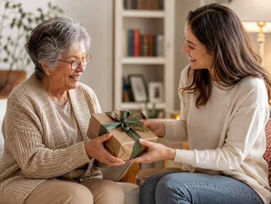 A woman presents a beautifully wrapped gift to her grandmother, who looks delighted and surprised